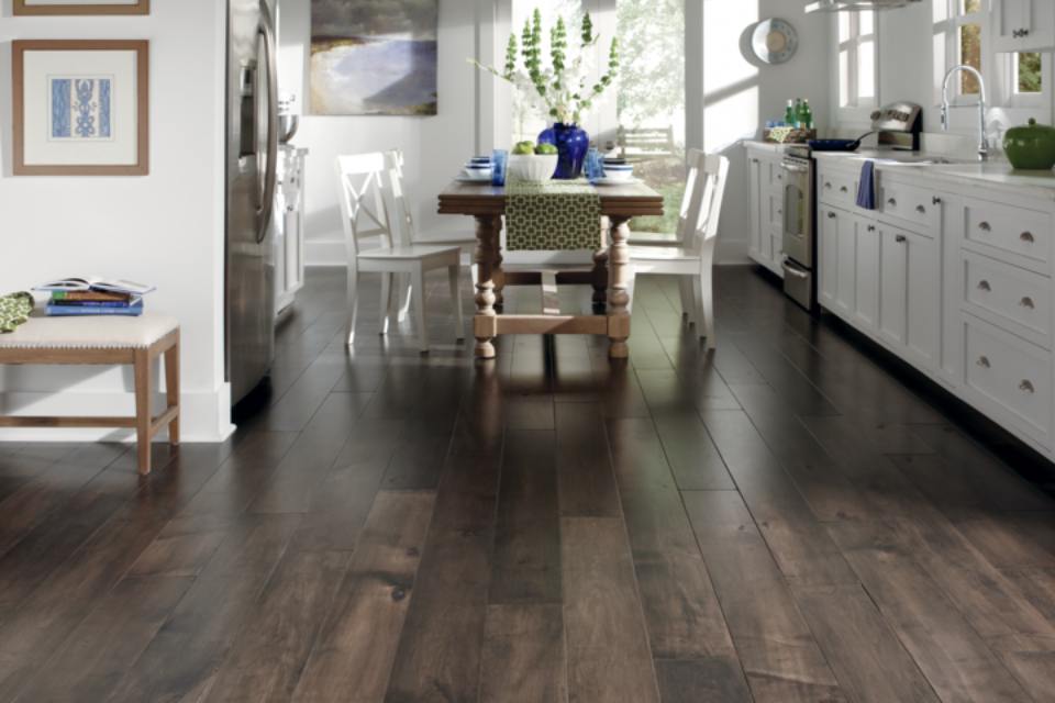 Dark hardwood flooring in kitchen with white cabinets and wood dining table.